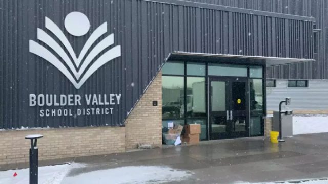 Exterior via of the Boulder Valley School District main entrance showing large logo on building to the left of glass doors with snow on the ground.