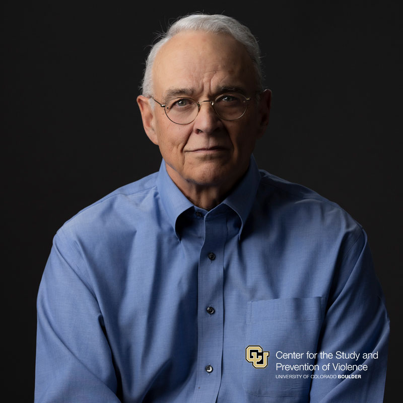 Headshot of a white man with short white hair wearing wire-framed glasses and cornflower blue button down shirt.