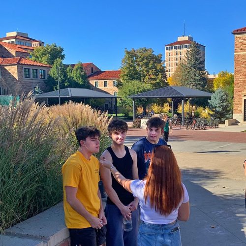 Red-haired white woman interviewing three white people all with short brown hair wearing casual clothing.