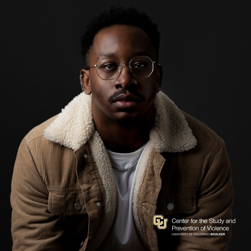 Headshot of a black man with short black hair wearing a tan sherpa jacket and white tee.