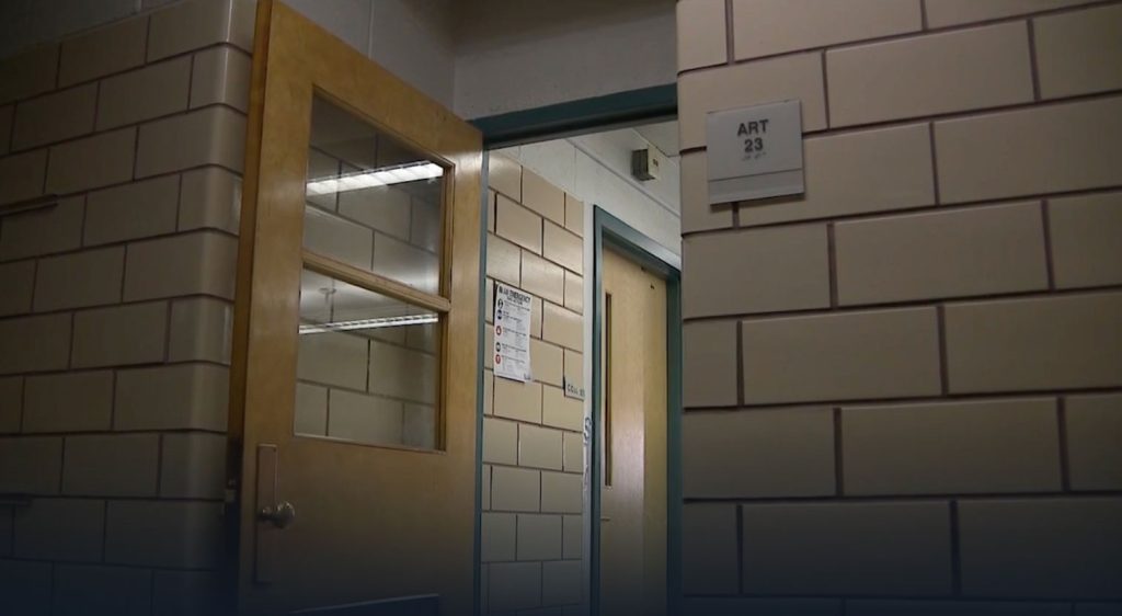 A classroom door stands open in a brick wall hallway of a school.