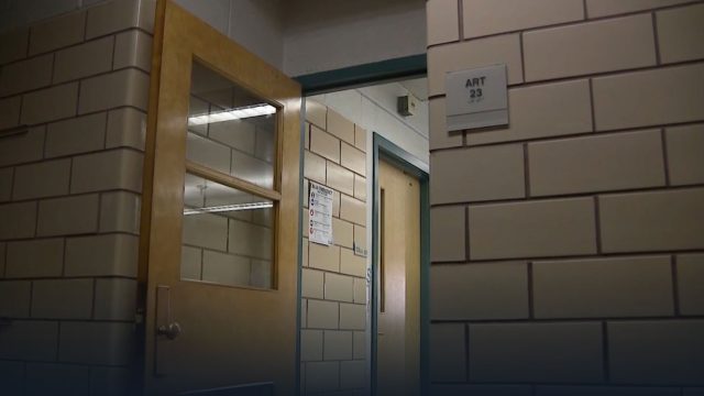 A classroom door stands open in a brick wall hallway of a school.