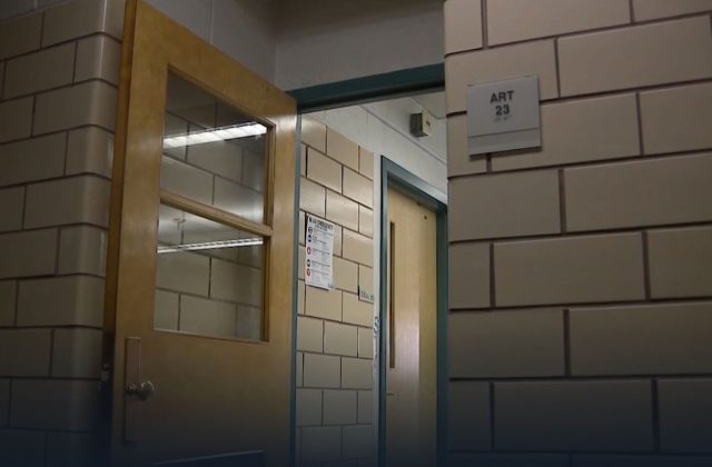 A classroom door stands open in a brick wall hallway of a school.